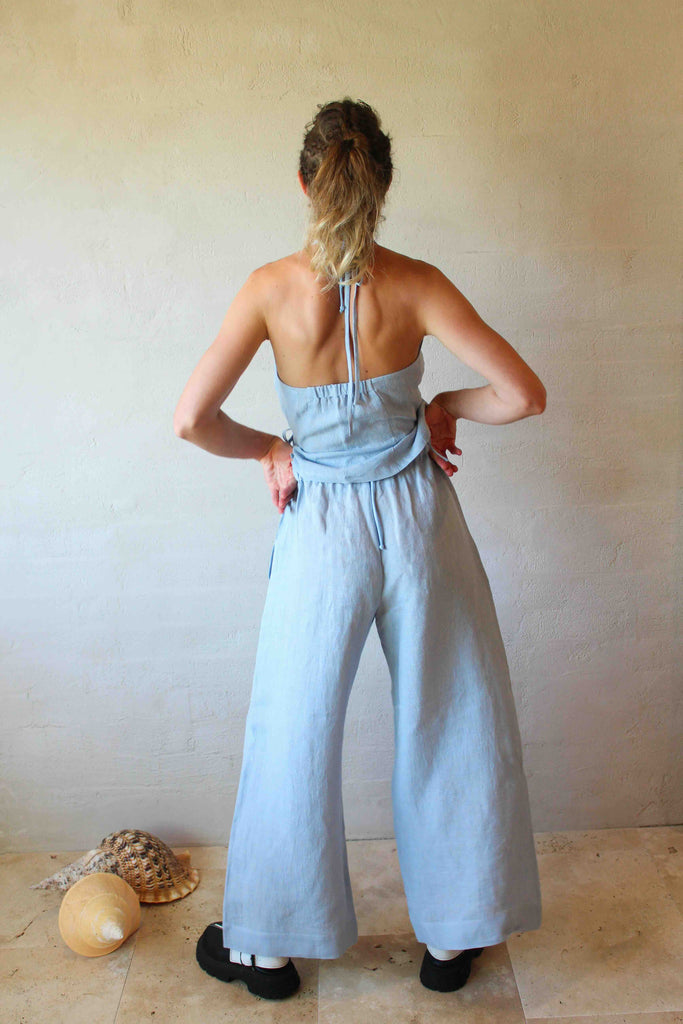 Woman wearing a light blue jumpsuit standing against a plain wall.
